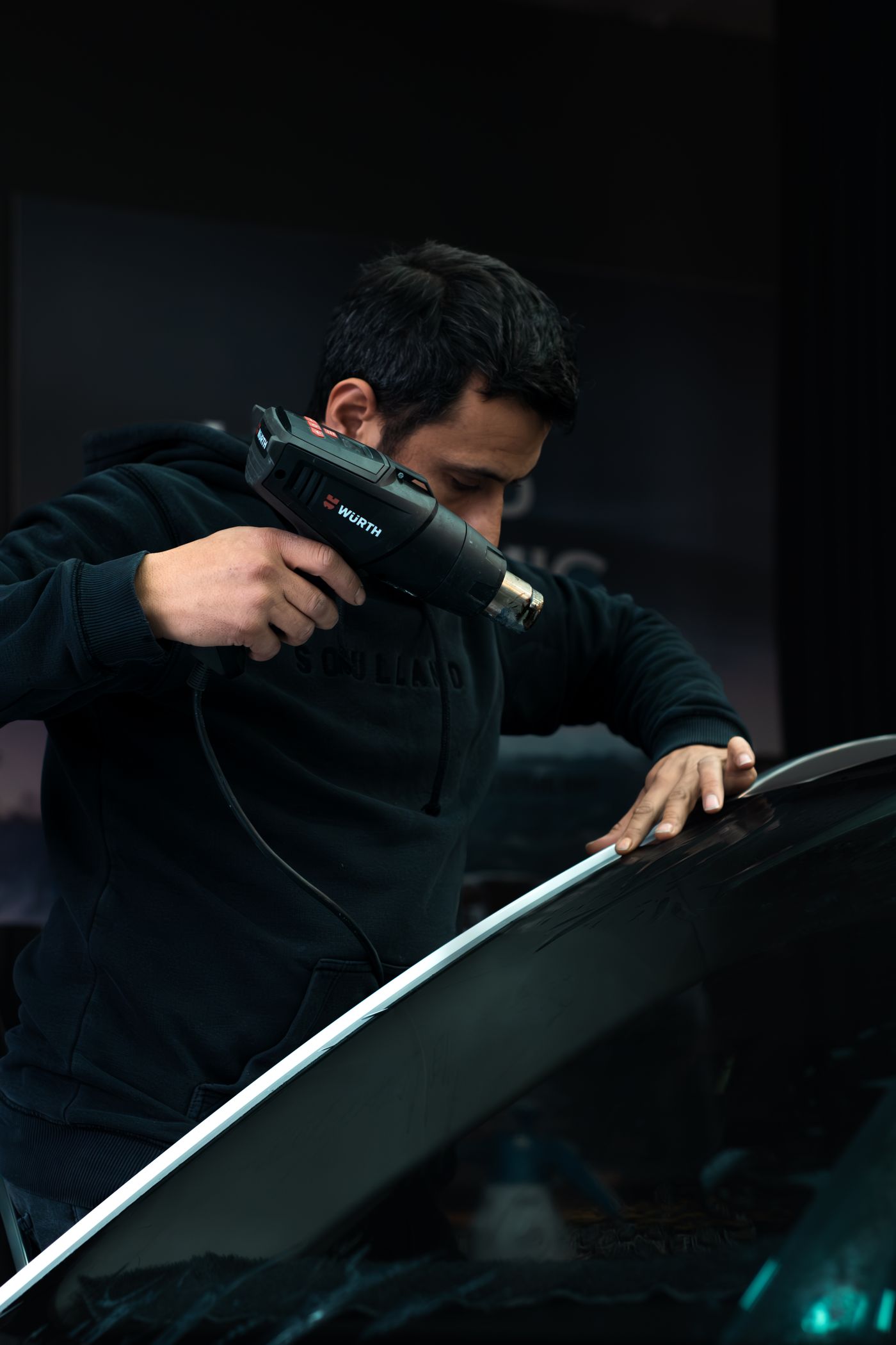 Auto glass technician working the edge of a windshield with a heat gun