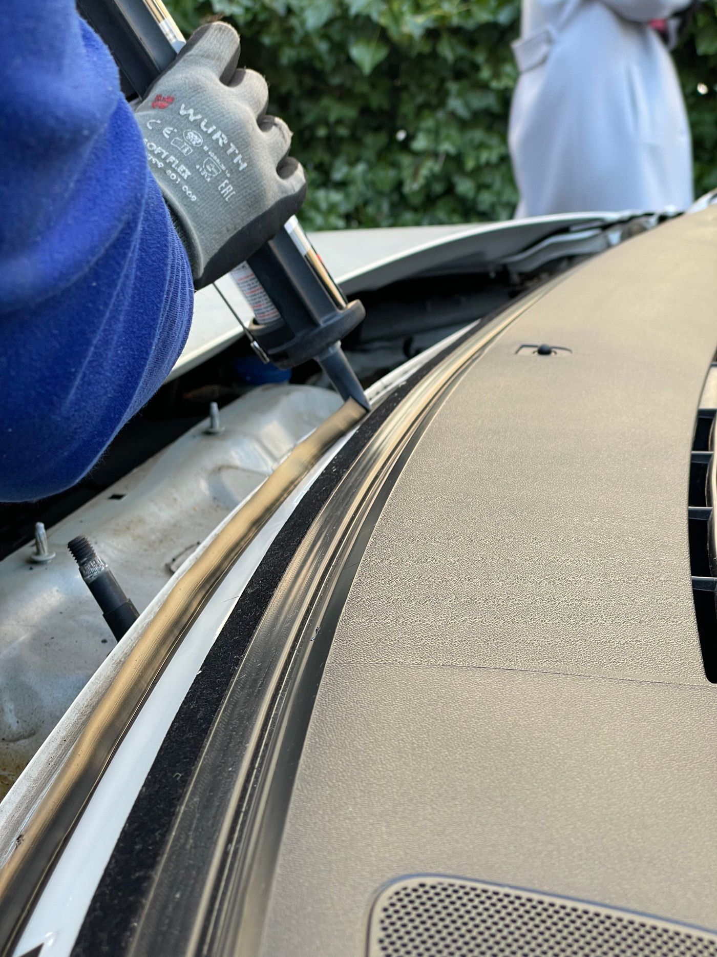 Auto glass technician running a urethane bead during a mobile windshield replacement in a customer driveway